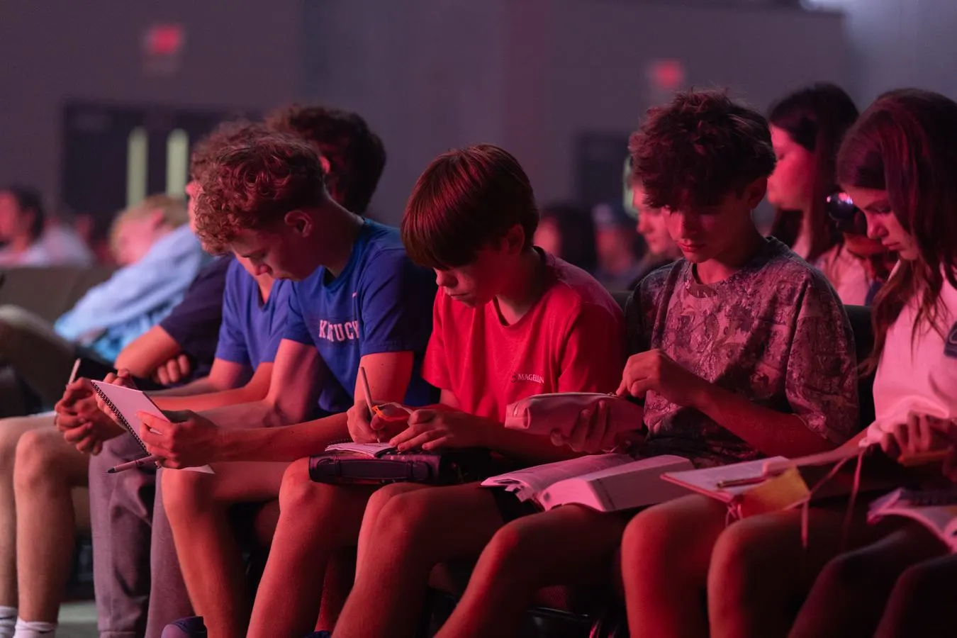 Students seated in a row, reading and taking notes in their Bibles